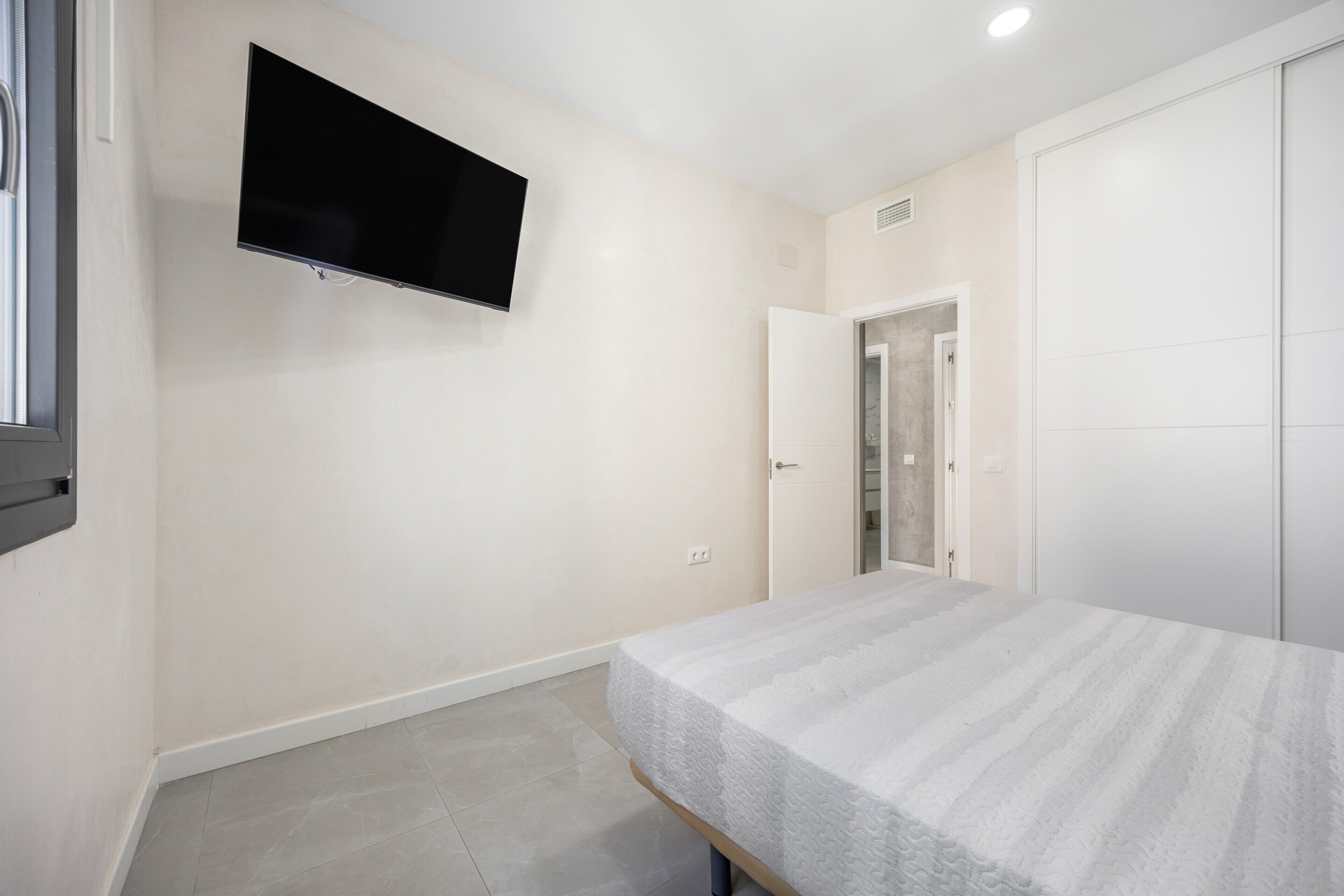 Una camera da letto con un letto, una televisione a muro e una porta che dà su un'altra stanza.