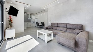 Una sala de estar moderna con un sofá gris, una mesa de centro blanca y un televisor de pantalla plana montado en la pared.
