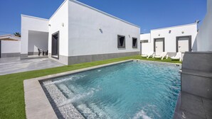 Un edificio moderno con piscina, un patio con sillas y un cielo azul despejado.