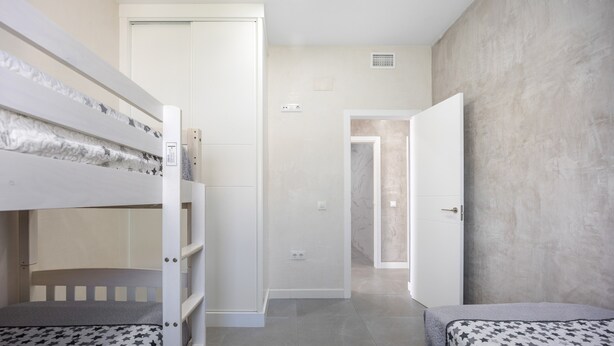 A bedroom with bunk beds, a door, and a hallway leading to another room.