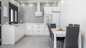 Una cocina moderna con muebles blancos, microondas, horno y zona de comedor con mesa y sillas.