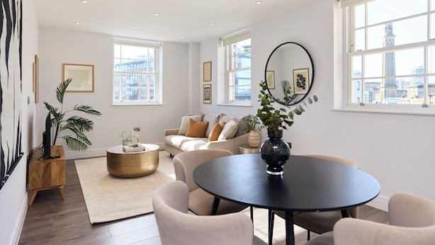 A modern living room with a round dining table, beige sofas, and a large window with a city view. - Second Storey at Kew (Brentford)