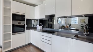 A modern kitchen with white cabinetry, a built-in oven, a microwave, and a stainless steel sink. - Second Storey at Kew (Brentford)