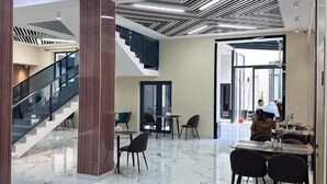 A modern hotel lobby with a marble floor, a staircase, and a dining area with tables and chairs. - North Star Hotel (Tashkent)