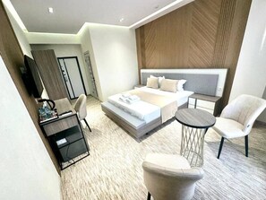 A modern hotel room with a large bed, a small round table, a sofa, and a TV on a stand. - North Star Hotel (Tashkent)