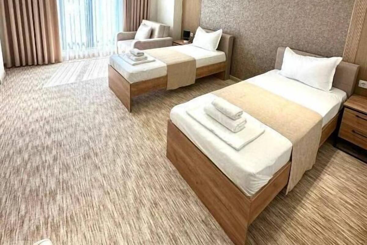 Habitación de hotel con dos camas, un sofá, un escritorio y un ventanal con cortinas.