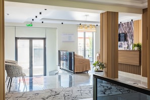 A hotel lobby with a reception desk, a seating area with a sofa, a glass railing, and a large window with a view of the outside. - North Star Hotel (Tashkent)
