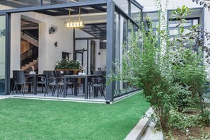 Un espacio moderno para comer al aire libre con paredes de vidrio, una mesa con sillas y un pequeño jardín.