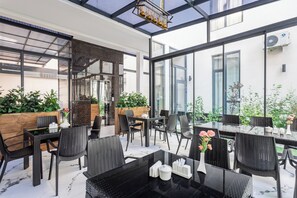 Un patio interior con paredes de vidrio, mobiliario de mimbre negro y plantas en macetas.