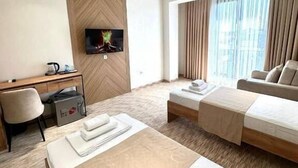 A hotel room with a bed, a sofa, a desk, a TV, and a window with curtains. - North Star Hotel (Tashkent)