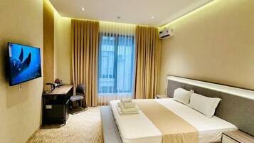 Een moderne hotelkamer met een groot bed, een bureau, een stoel, een televisie en een raam met gordijnen.