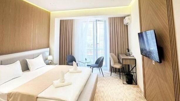 A modern hotel room with a large bed, a desk, a chair, a TV, and a window with curtains. - North Star Hotel (Tashkent)