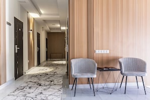 A hotel corridor with a marble floor, wooden panel walls, and a seating area with two chairs and a table. - North Star Hotel (Tashkent)