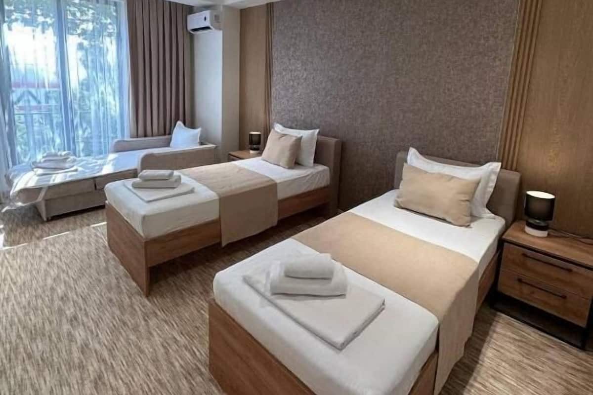 Habitación de hotel con dos camas, un sofá, una mesita de noche y una ventana con cortinas.