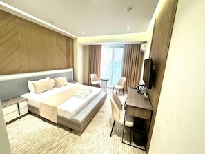 A modern hotel room with a large bed, a desk, and a chair. There is a small table and a chair in the corner. - North Star Hotel (Tashkent)
