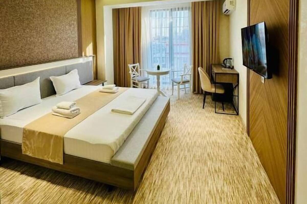 Habitación de hotel con una cama grande, un escritorio, una silla, un televisor y una ventana con cortinas.