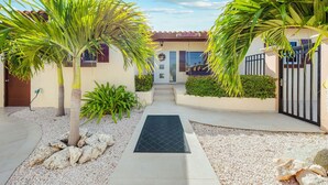 Une maison moderne avec une allée pavée, des palmiers et une entrée fermée par un portail.