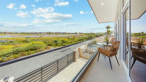 Un balcon donnant sur une route et sur un espace verdoyant, aménagé avec des chaises et une table.