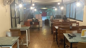 Interior de restaurante con suelo de madera, mesas y sillas dispuestas para comer.