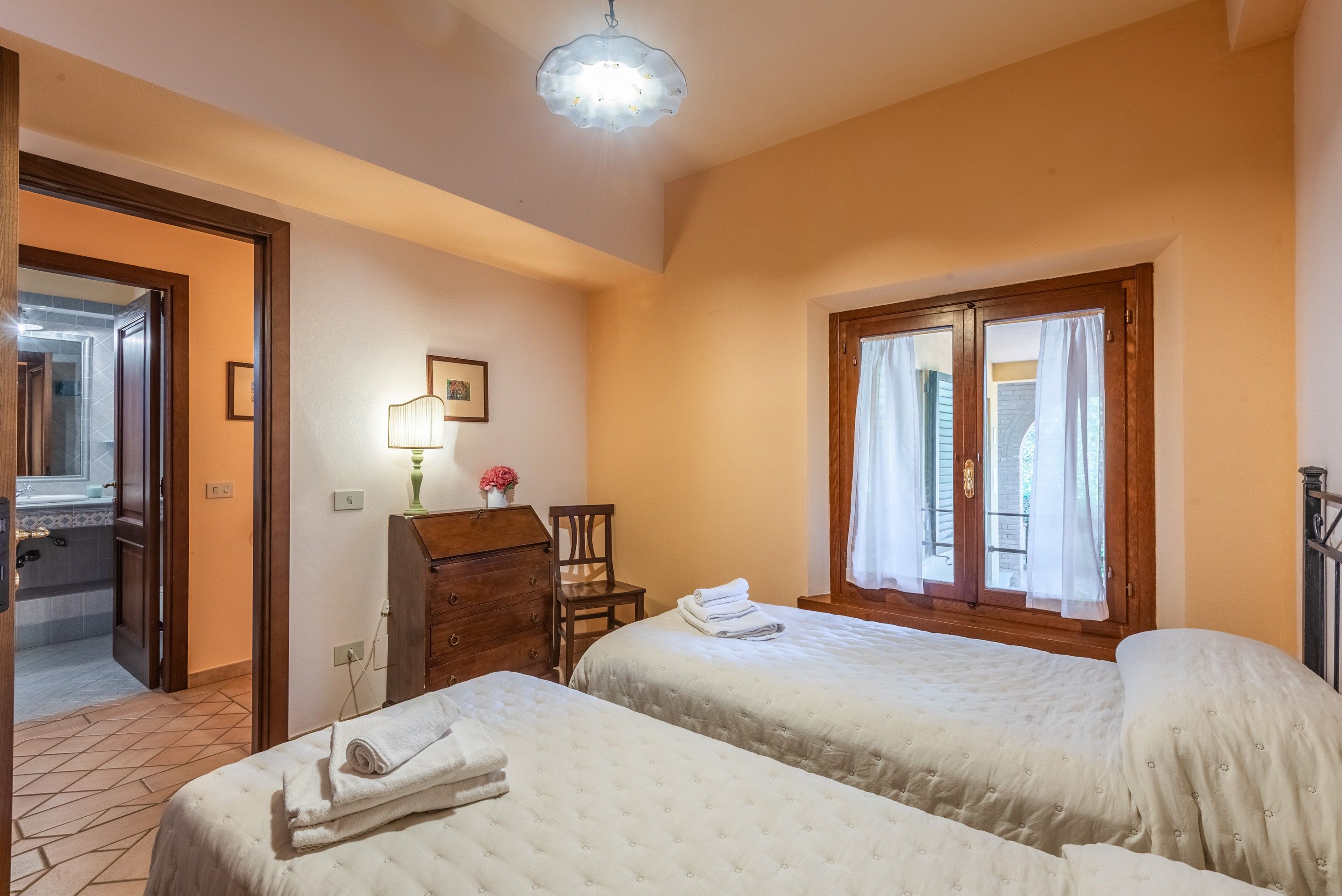 Une chambre d’hôtel avec deux lits, un bureau avec une lampe, une chaise et une fenêtre avec des rideaux.