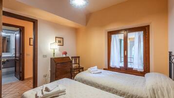 Une chambre d’hôtel avec deux lits, un bureau avec une lampe, une chaise et une fenêtre avec des rideaux.