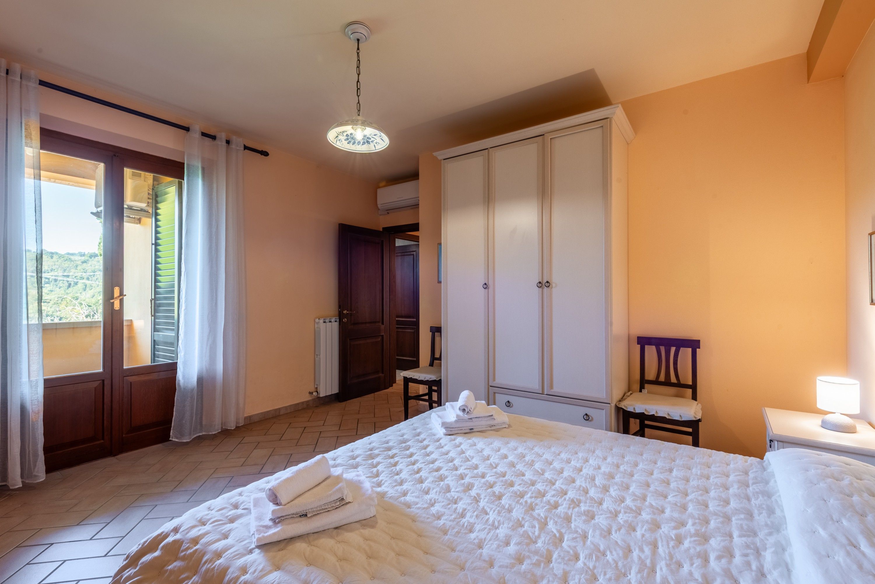 Une chambre d’hôtel avec un lit, une armoire, une chaise, une table et une fenêtre avec des rideaux.