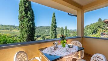 A balcony with a table set for two, overlooking a scenic landscape with trees and hills.