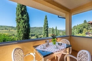 Ein Balkon mit Tisch für zwei Personen, mit Blick auf eine malerische Landschaft aus Bäumen und Hügeln.