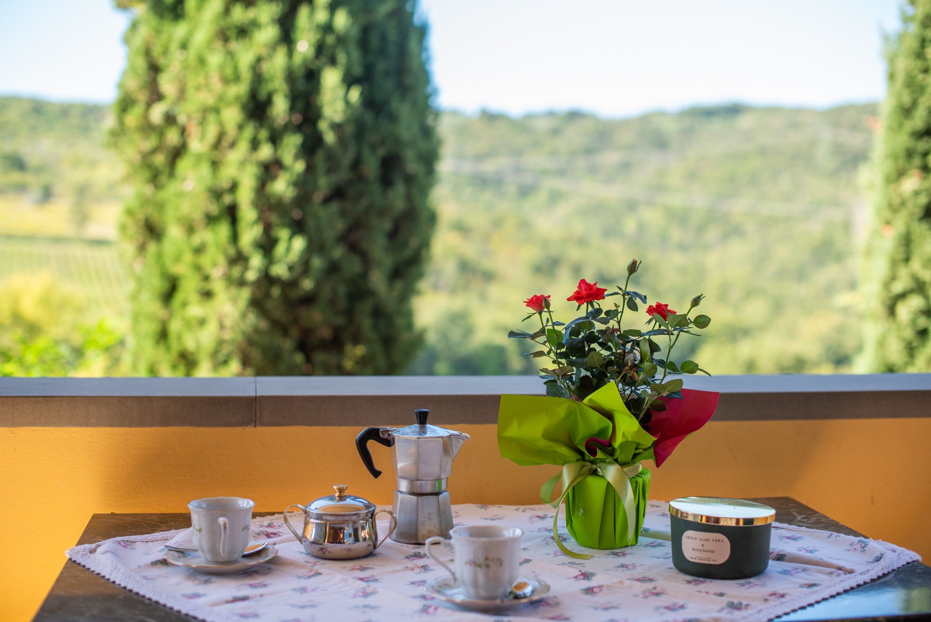 Ein Tisch mit einer Kaffeekanne, Tassen, einer Blumenvase und einer Kerze.