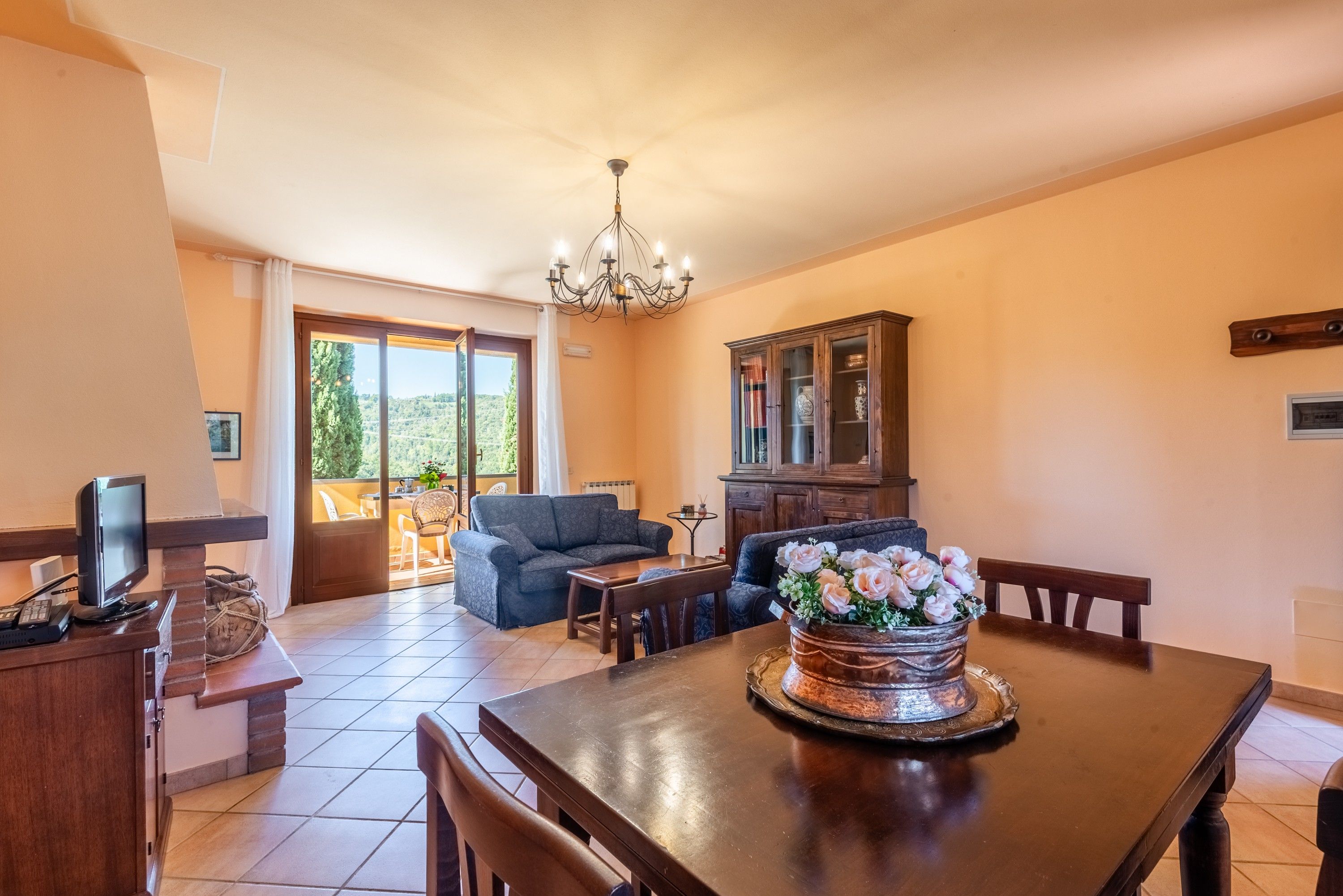 A dining area with a wooden table, chairs, a chandelier, and a cabinet with glass doors.