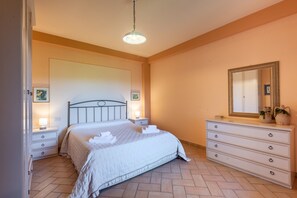A bedroom with a bed, bedside tables, a dresser, a mirror, and a hanging light fixture.