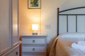 Ein ordentlich bezogenes Bett mit Kopfteil, ein Nachttisch mit Lampe und ein an der Wand befestigter Lichtschalter.