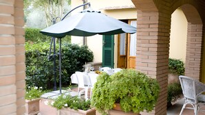 Un patio al aire libre con una mesa lista para comer, plantas en macetas y una silla blanca.