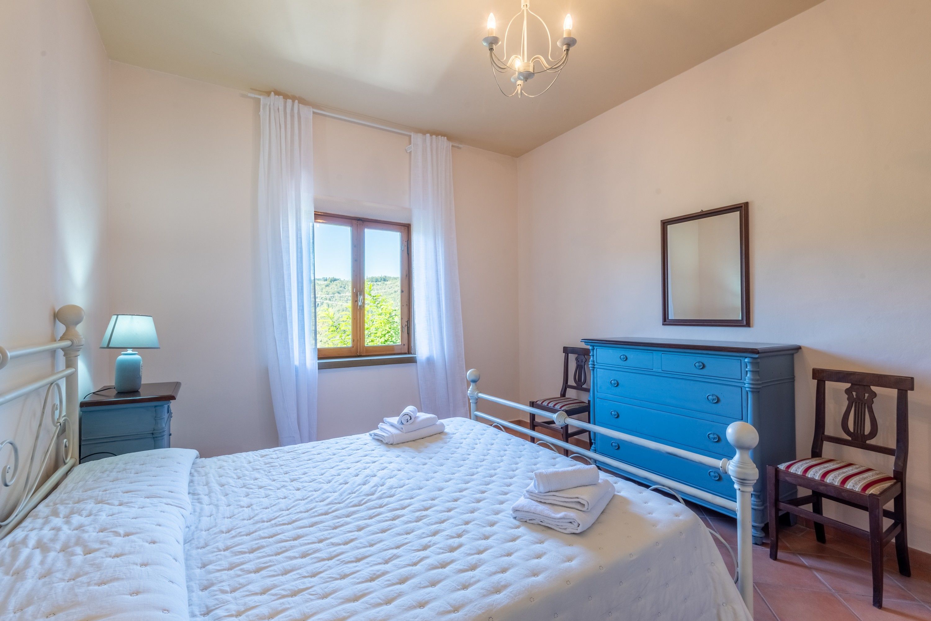 Une chambre à coucher comprenant un lit, une commode, une chaise, une fenêtre avec des rideaux et un lustre.