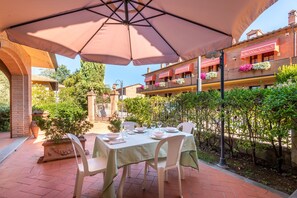 An outdoor dining area with a table set for two under a large umbrella, surrounded by brick walls and greenery. - Agriturismo I Borghi – Apartment Tabacco with Pool in San Gimignano (San Gimignano)