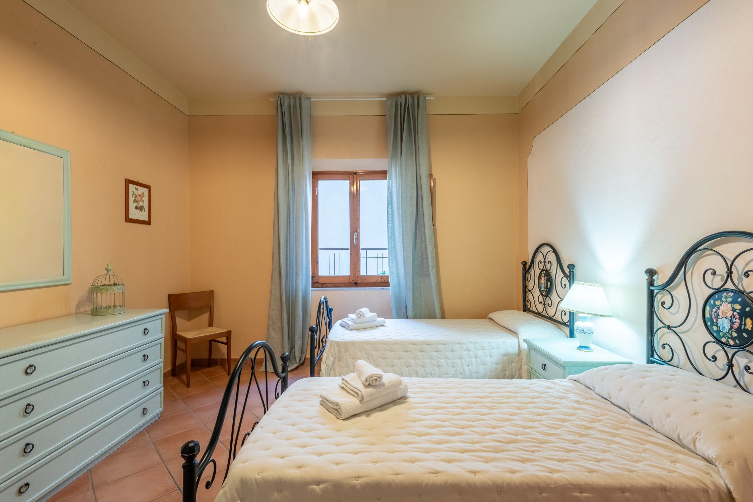 A bedroom with two beds, a dresser, a chair, and a window with curtains.
