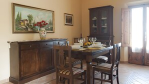 Comedor con una mesa de madera dispuesta para cuatro, sillas, un aparador y dos cuadros en la pared.