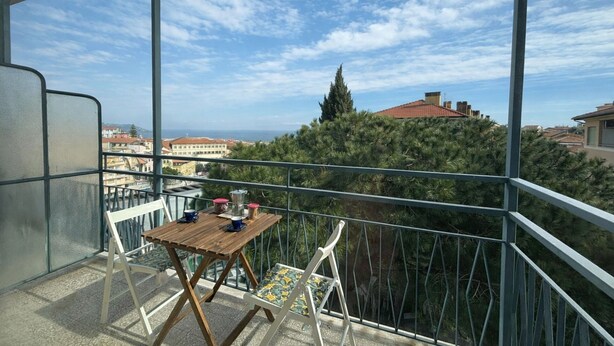Een balkon met een tafel en stoelen, met uitzicht op een stadsgezicht en een boom.
