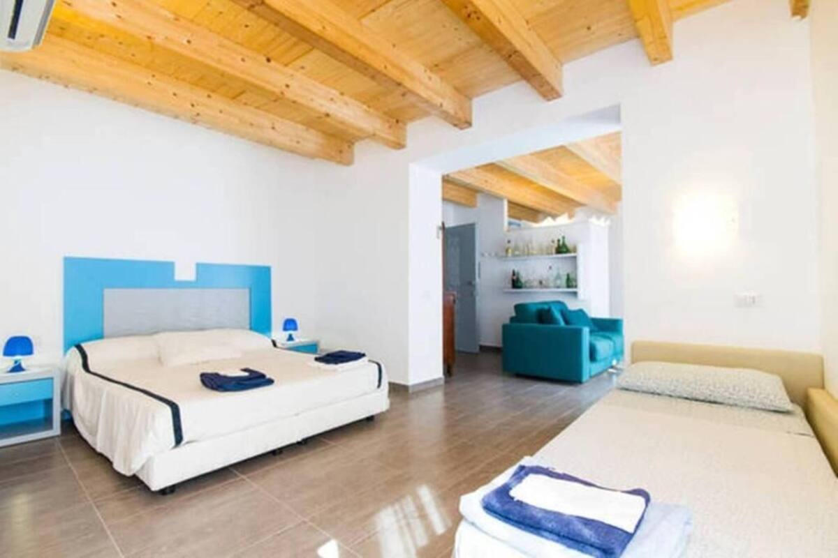 A bedroom with a bed, a nightstand, a blue chair, and a sofa.