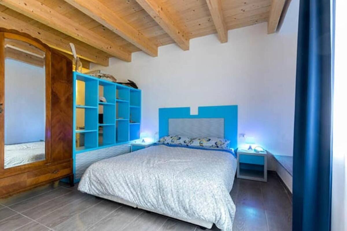 A bedroom with a wooden ceiling, a bed with a white bedspread, a blue headboard, and a blue shelving unit.