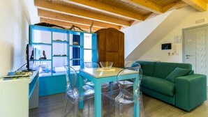 Una habitación con una mesa y sillas azules, un sofá verde y techo de madera.