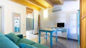 Una sala de estar moderna con un sofá verde, techo de madera y un comedor con mesa y sillas azules.