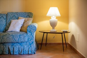 Una habitación con un sofá estampado, una mesa con una lámpara y un piso de baldosas.