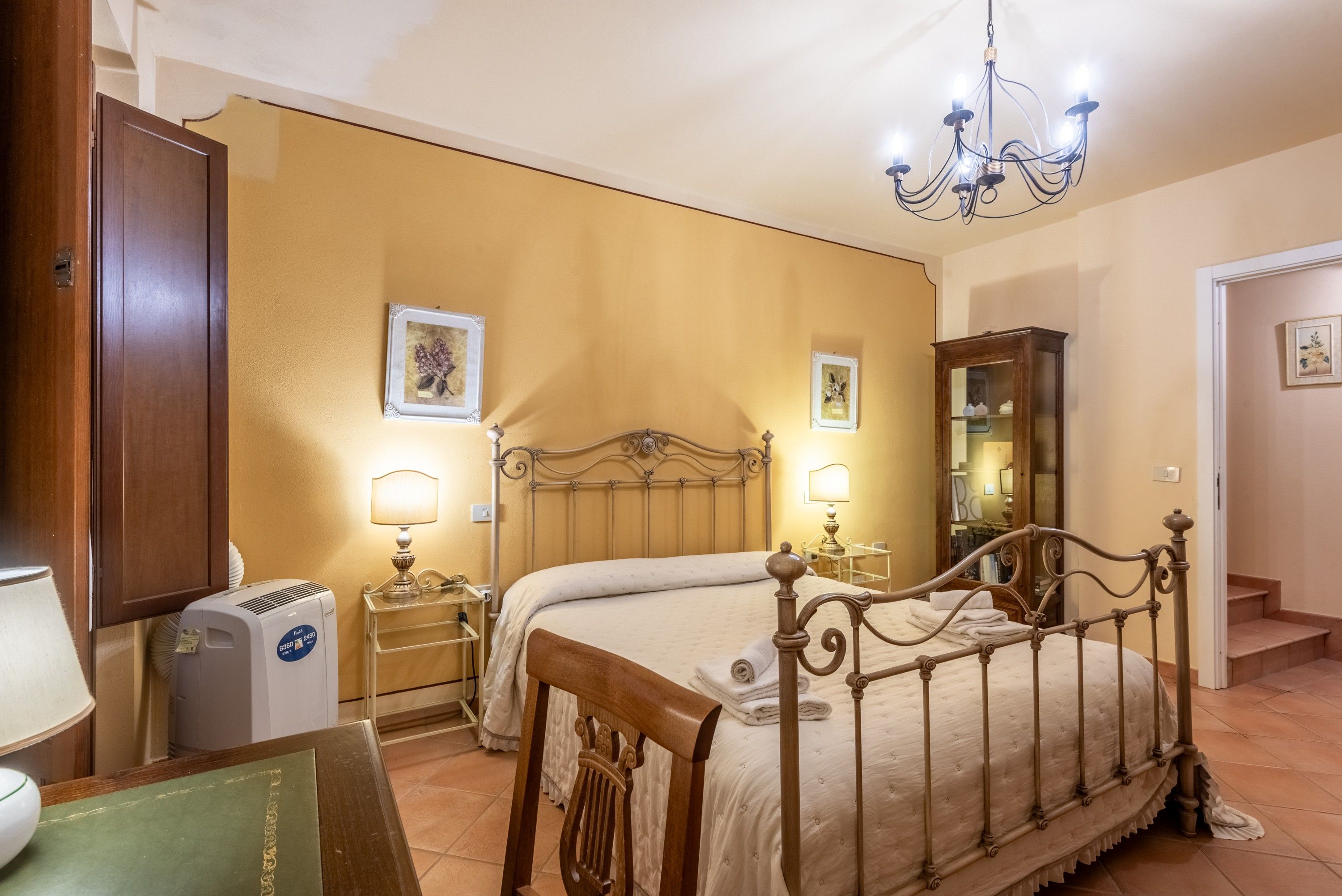 A bedroom with a bed, bedside lamps, a heater, a mirror, and a chandelier.