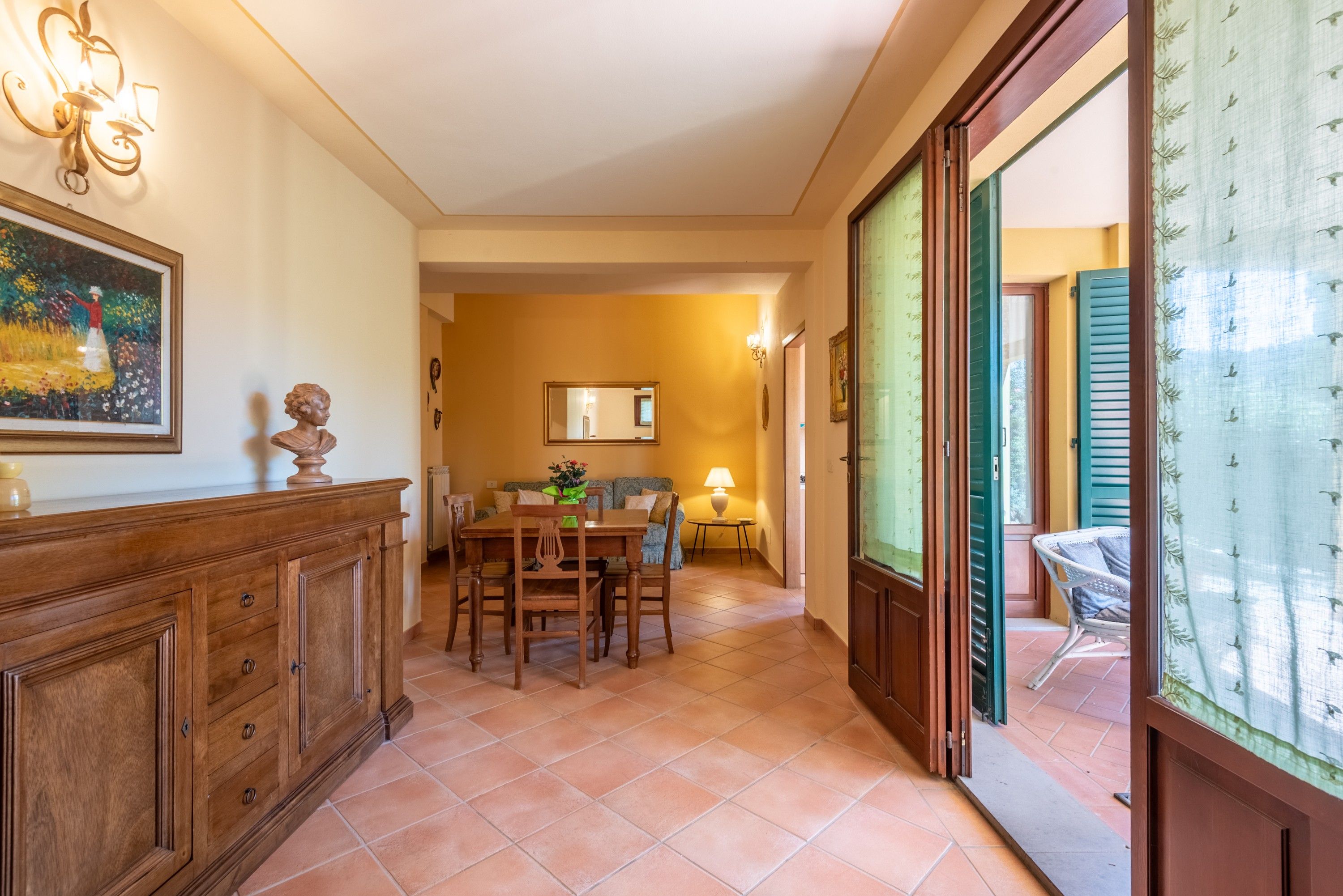 A dining area with a wooden table and chairs, a mirror on the wall, and a view through an open door.