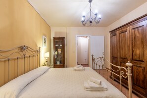 Un dormitorio con cama, un armario de madera, una araña y una puerta que da a otra habitación.