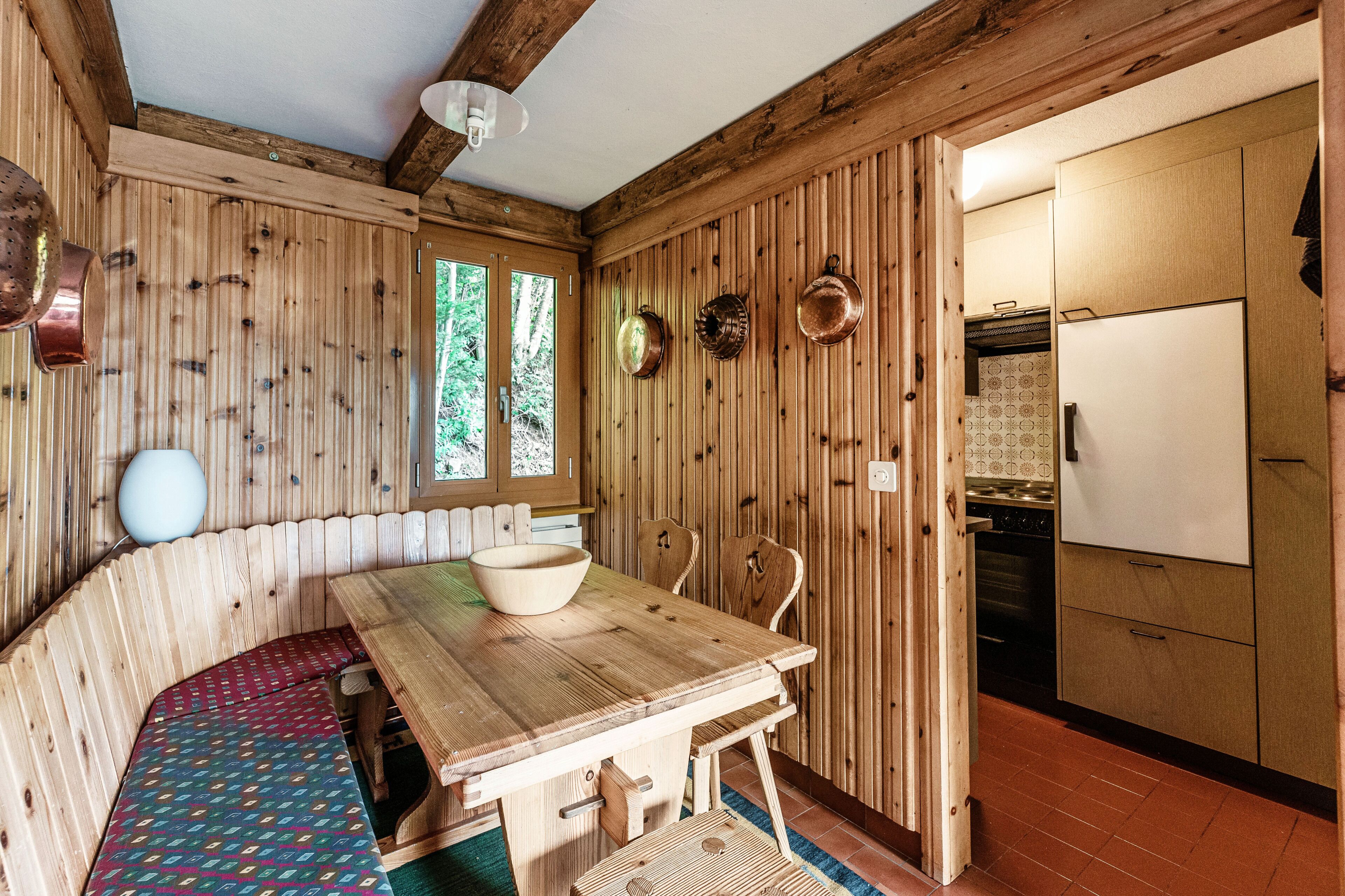 A wooden interior with a dining table, benches, and a kitchen area.