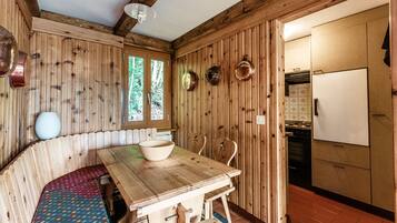 A wooden interior with a dining table, benches, and a kitchen area.