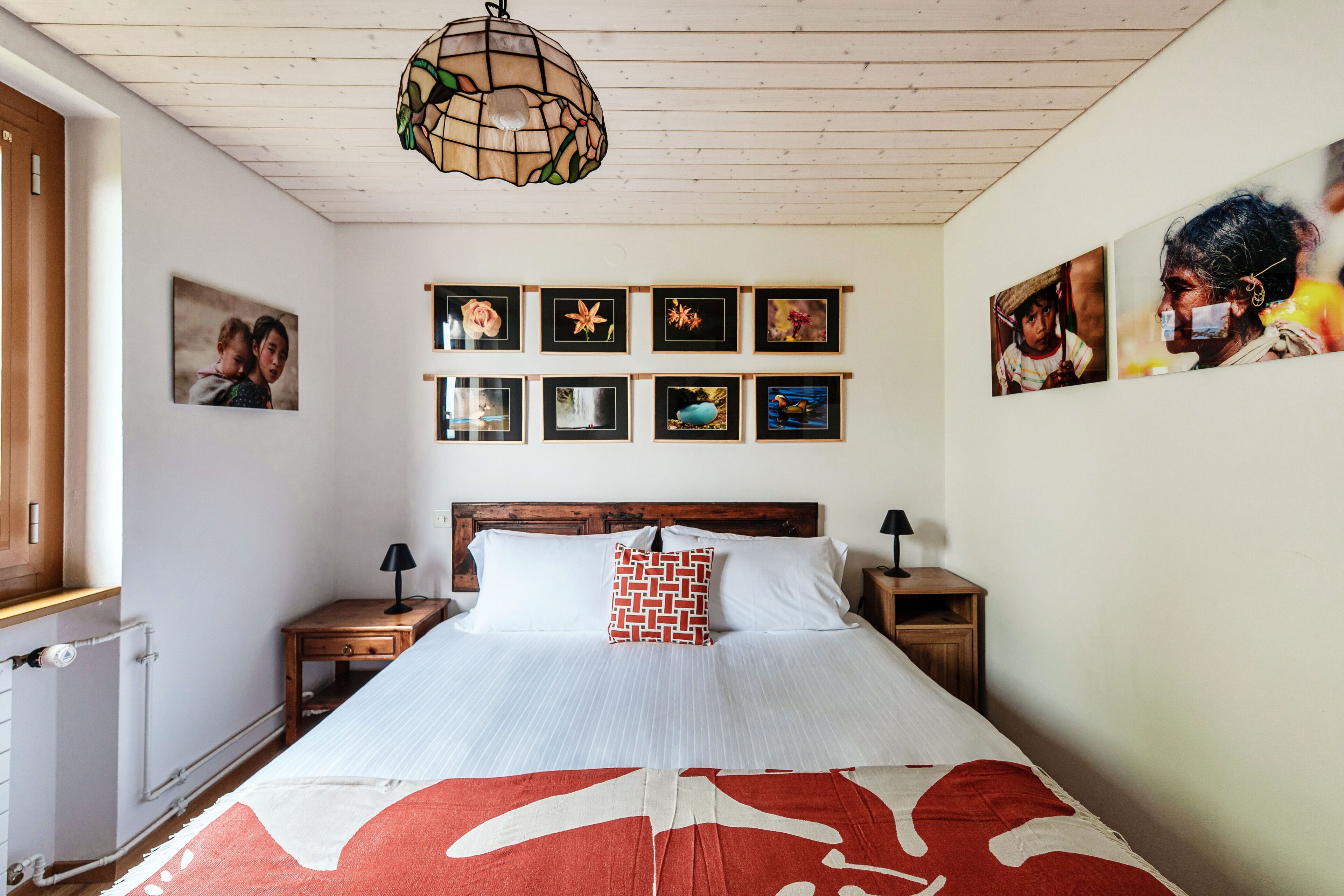 A bedroom with a bed, a wooden headboard, a hanging light fixture, and framed pictures on the wall.