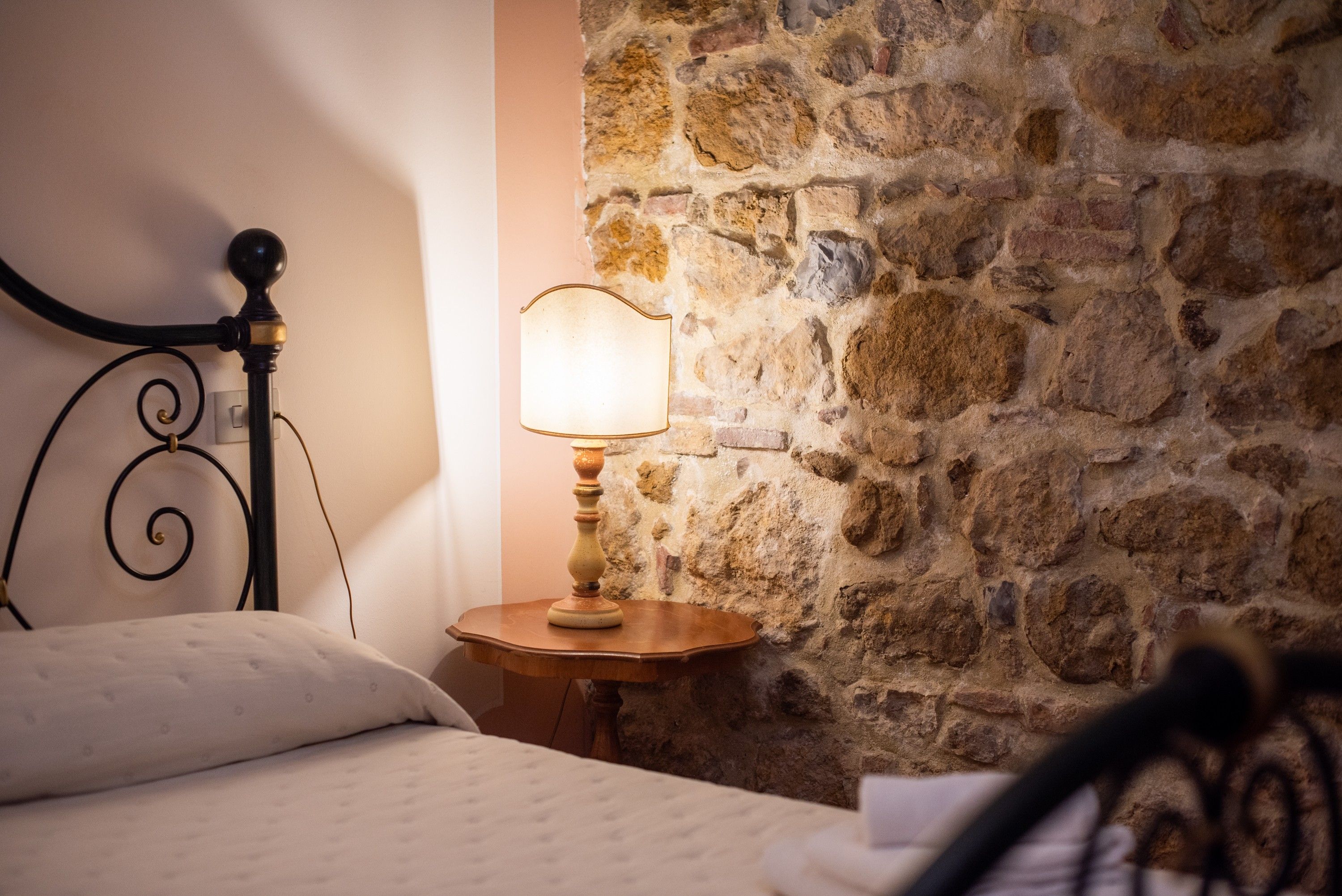 A bed with a headboard, a bedside lamp, and a stone wall.